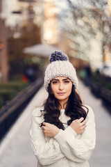 Wall Mural - Elegant girl walk in a winter city. Woman in a white knited sweater. Beautiful lady with dark hair.