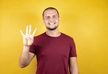 Russian man wearing basic red t-shirt over yellow insolated background showing and pointing up with fingers number four while smiling confident and happy.