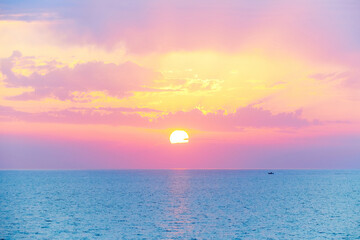 Spectacular beautiful sunset or sunrise on the mediterranean sea. Beautiful pink orange purple yellow light filters through the clouds. A small dinghy boat sails at the horizon on the turquoise sea