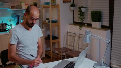 Poster - Businessman writing notes while working late on computer in home kitchen. Busy focused employee using modern technology network wireless doing overtime for job reading typing, searching