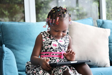 Wall Mural - African American kid is homeschooling by learning from digital tablet while sitting on sofa couch at home