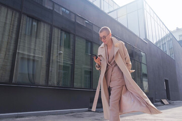 Smart attractive woman with short hair. A businesswoman using her smartphone and smiles on a city street.