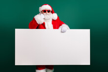 Photo Of Retired Confident Grandpa Hold White Empty Board Offer Incredible Newyear Proposition Wear Red Santa Costume Coat Gloves Sunglass Headwear Isolated Green Color Background