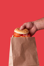 The Delivery Guy Puts A Burger In A Craft Eco Bag. Red Background.