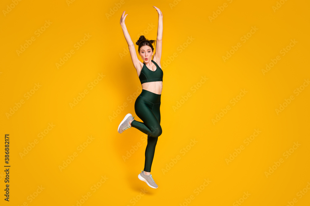 Full size photo of sportive lady jump high up active person raise arms wear sports suit sneakers isolated yellow color background - obrazy, fototapety, plakaty 