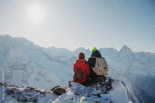 A loving couple of travelers with backpacks from the back look at the snowy mountains. Vacation in the mountains.