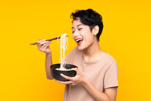Young Asian Girl Over Isolated Yellow Background Holding A Bowl Of Noodles With Chopsticks And Eating It