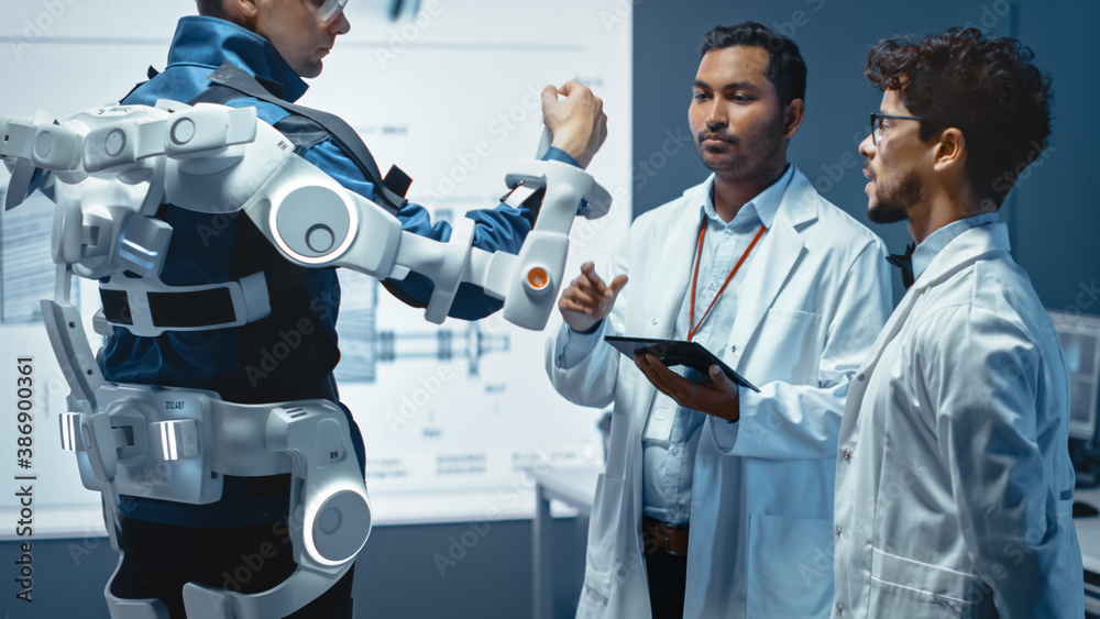 In Robotics Development Laboratory: Engineers and Scientists Work on a Bionics Exoskeleton Prototype with Person Testing it. Designing Wearable Exosuit to Help Disabled People. - obrazy, fototapety, plakaty 