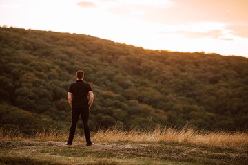 Back view of  a young caucasian man standing on a mountain at sunset. A beautiful day in the fresh mountain air