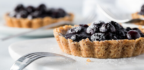 Wall Mural - Close up front facing view of a blueberry tartlet with another in soft focus in behind.