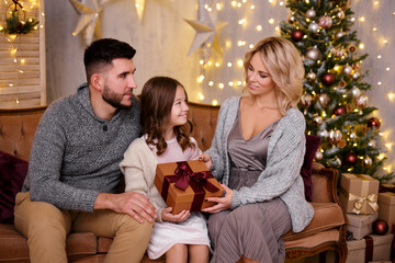 Wall Mural - parents giving present to their daughter in living room with decorated Christmas tree