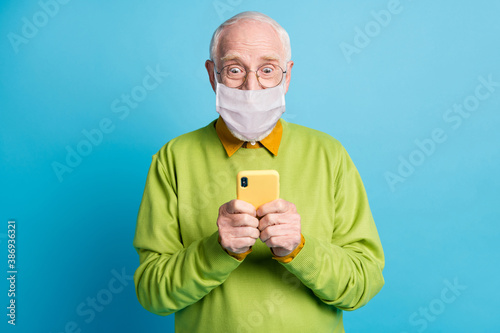 Photo of excited grandpa hold telephone look screen wear white face mask isolated blue color background