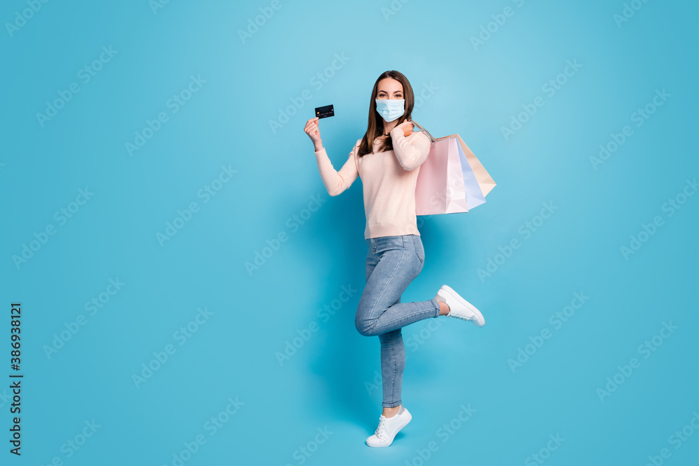 Full length view of girl jumping carrying new things credit card wear mask isolated shine vibrant blue color background - obrazy, fototapety, plakaty 
