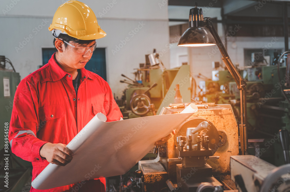 Machine Foreman Asian man foreman working with drawing and NC Lathe machinery with ...
