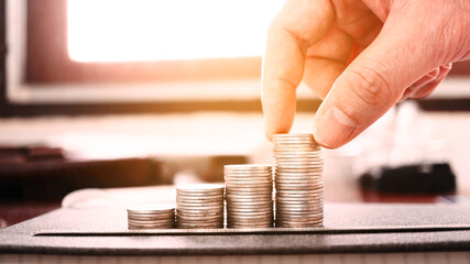 Hand pick up stack of coins which decorate on working table with sunlight from window background  , financial discipline concept.