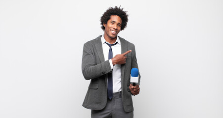 Wall Mural - young black afro man smiling cheerfully, feeling happy and pointing to the side and upwards, showing object in copy space