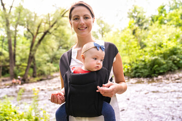 Young beautiful caring mother holding her baby child in a sling walking on nature