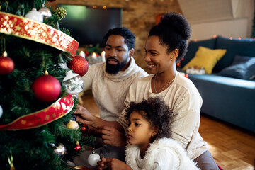 Wall Mural - Happy African American parents and their daughter decorating Christmas tree at home.