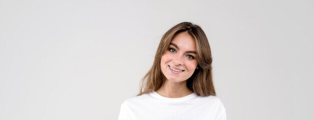 Wall Mural - Close up portrait of a beautiful young woman smiling looking to the camera isolated on white background. Banner size, empty space