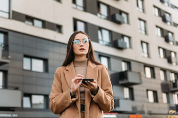 Wall Mural - Business woman brunette girl using mobile phone near office, beautiful woman browsing phone and doing online shopping in a mobile app while smiling walking near shopping mall.