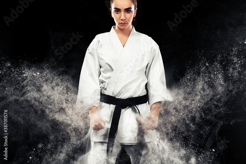 Fotografering Portrait of sporty karate and taekwondo woman in white kimono with black belt on dark background