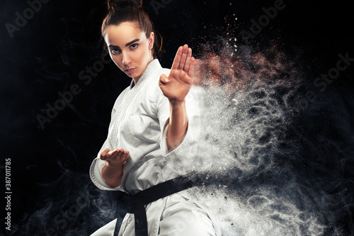 Fotografering Portrait of sporty karate and taekwondo woman in white kimono with black belt on dark background
