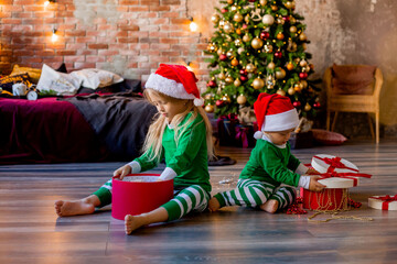 Wall Mural - Two young children in pajamas and Santa hats unpack Christmas presents in the room