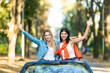 Young two women raising hands in convertible car