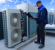 air conditioning technician making a diagnosis of an industrial air conditioning unit with a laptop next to other VRV condenser units on a rooftop in a sunny day