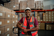 Male Factory Worker Smiling Besides Packages In Warehouse 