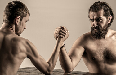 Wall Mural - Arms wrestling thin hand, big strong arm in studio. Two man's hands clasped arm wrestling, strong and weak, unequal match. Heavily muscled bearded man arm wrestling a puny weak man