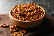 Wooden bowl with tasty cracker pretzels on napkin on black smokey background