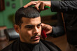 African-American barber's hand uses razor and haircut on Hispanic Latino man with goatee in a barbershop