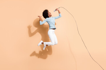 Photo portrait of excited african american woman singing holding mic in one hand in air isolated on pastel beige colored background