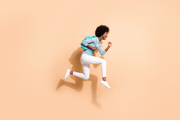 Wall Mural - Photo portrait of black skinned woman hurrying running jumping up with blue rucksack isolated on pastel beige colored background