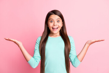 Photo of positive cute pretty small latin lady long hairdo raise hands hold empty space demonstrate propositions excited smile wear turquoise sweatshirt isolated pink color background