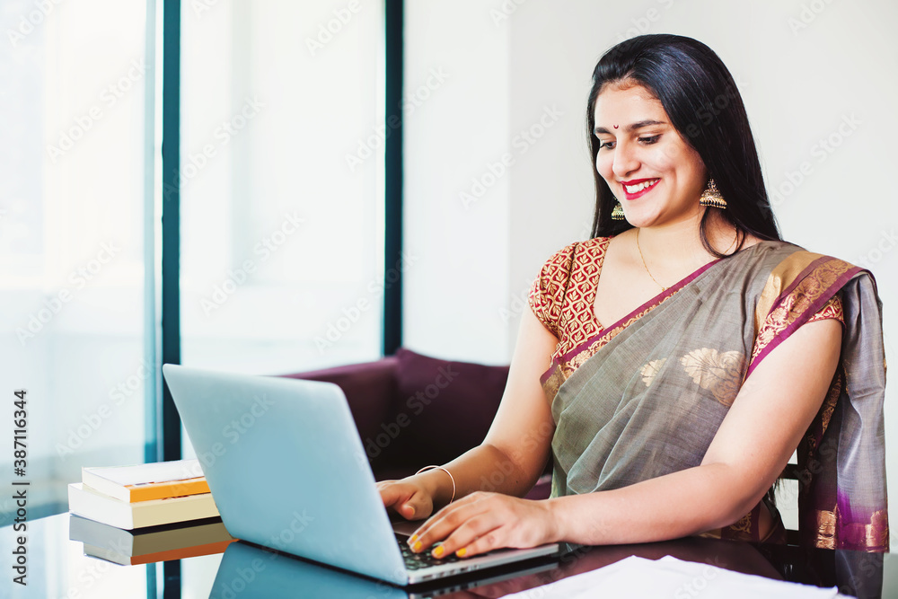 Beutiful Indian woman in a saree working on her laptop from ...