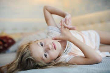 beautiful little idle lazy girl with blonde hair lying on bed at home relaxing at morning