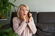 © JENOCHE - woman in a phone call sitting on a sofa in the living room in a house