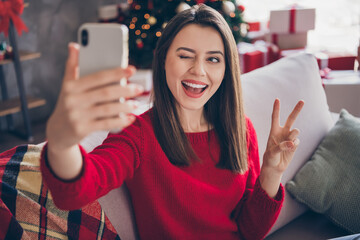 Sticker - Positive girl sit couch take selfie on smartphone make v-sign blink in house indoors with x-mas christmas ornament