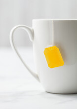 Teabag With Yellow Blank Tag Of Black Tea In White Porcelain Cup On White