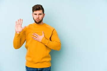 Wall Mural - Young caucasian man isolated on blue background taking an oath, putting hand on chest.