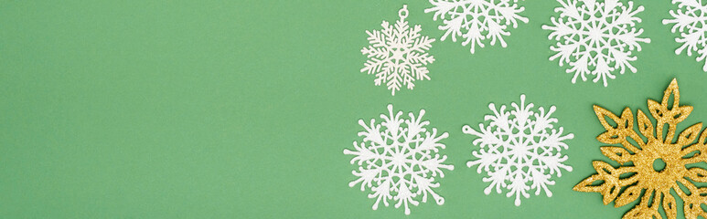 Canvas Print - panoramic crop of decorative white and golden snowflakes on green background with copy space