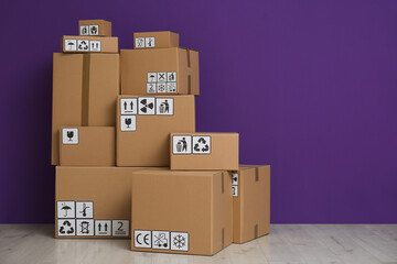 Wall Mural - Cardboard boxes with different packaging symbols on floor near purple wall, space for text. Parcel delivery