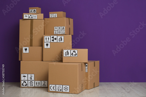 Cardboard boxes with different packaging symbols on floor near purple wall, space for text. Parcel delivery