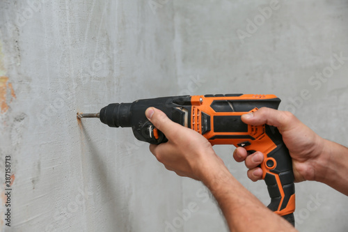 Cuadros en Lienzo person holds hammer drill close up on gray wall background