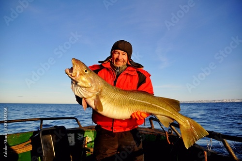 Fotografía A happy fisherman in a red jacket caught and holds in his hands a beautiful huge