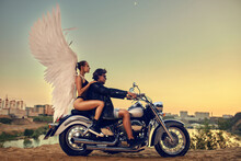 young beautiful couple stylishly dressed on a motorcycle at sunset, on a woman angel wings, guardian angel, dangerous driving
