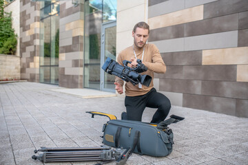 Wall Mural - Fair-haired operator standing on one knee, taking camera out of the case