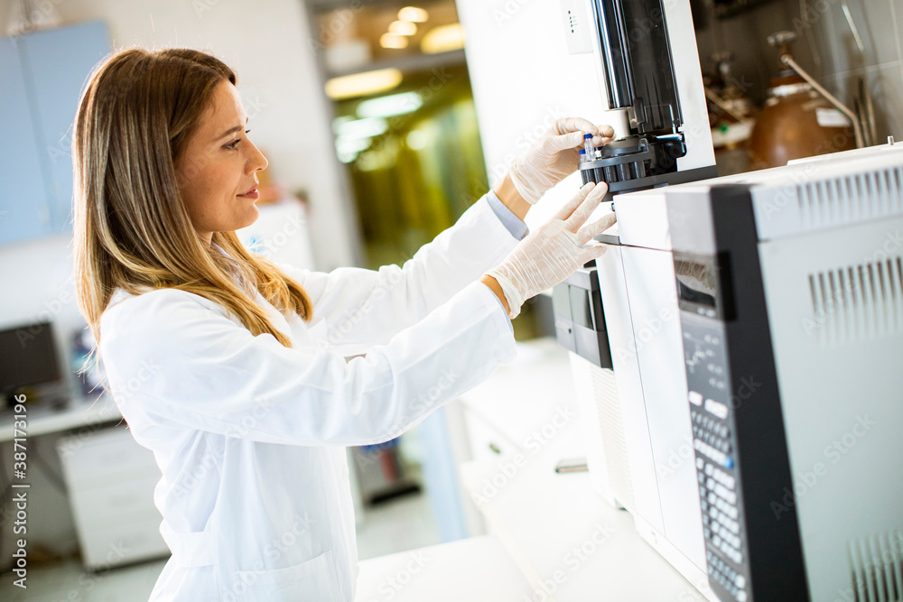 Female scientist in a white lab coat putting vial with a sample for an ...